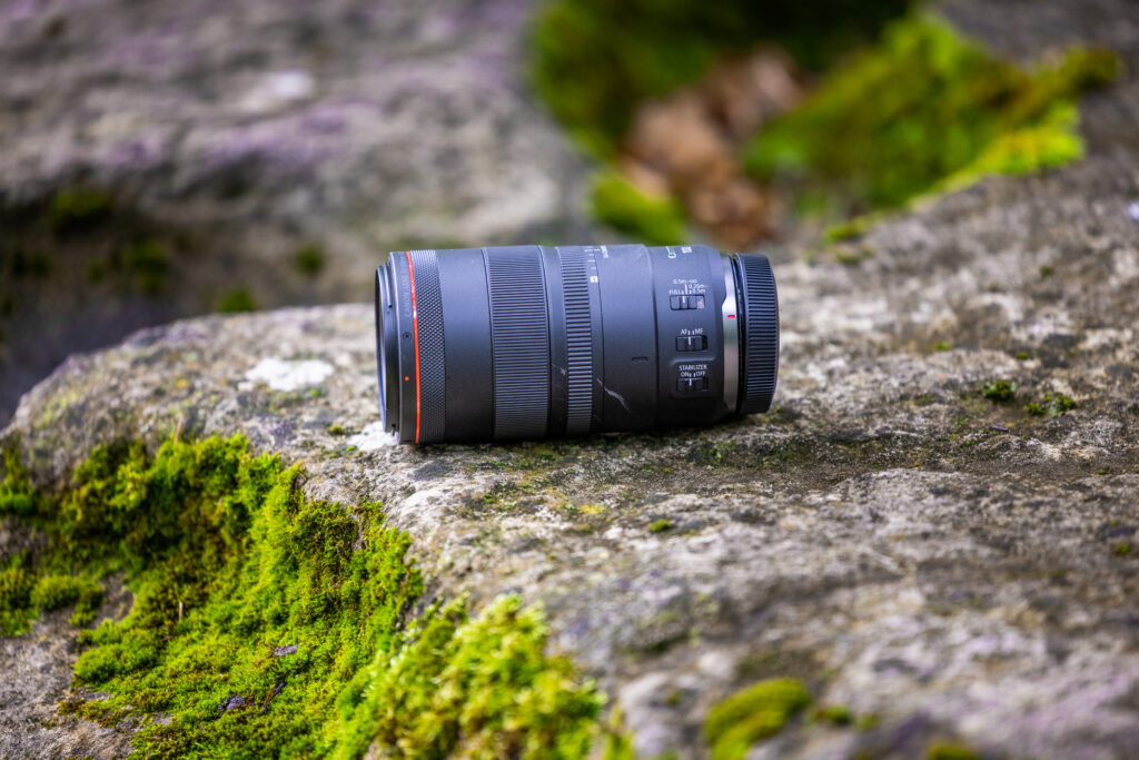 The Canon RF 100 F2.8 L lense on a mossy stone from the side.
