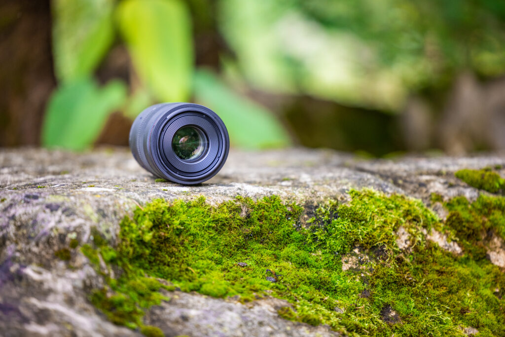 The Canon RF 100 F2.8 L lense on a mossy stone in a front shot.