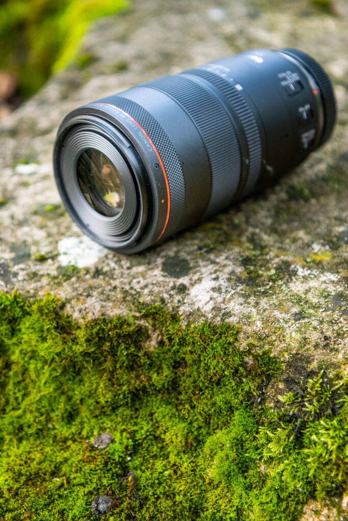 The Canon RF 100 F2.8 L lense on a mossy stone in a side shot.